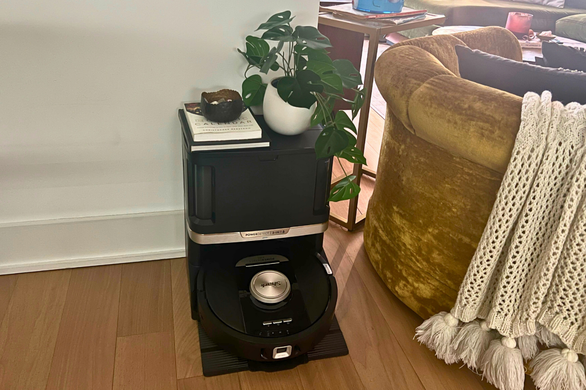 Shark PowerDetect robot vacuum and self-empty dock sitting against wall by yellow chair