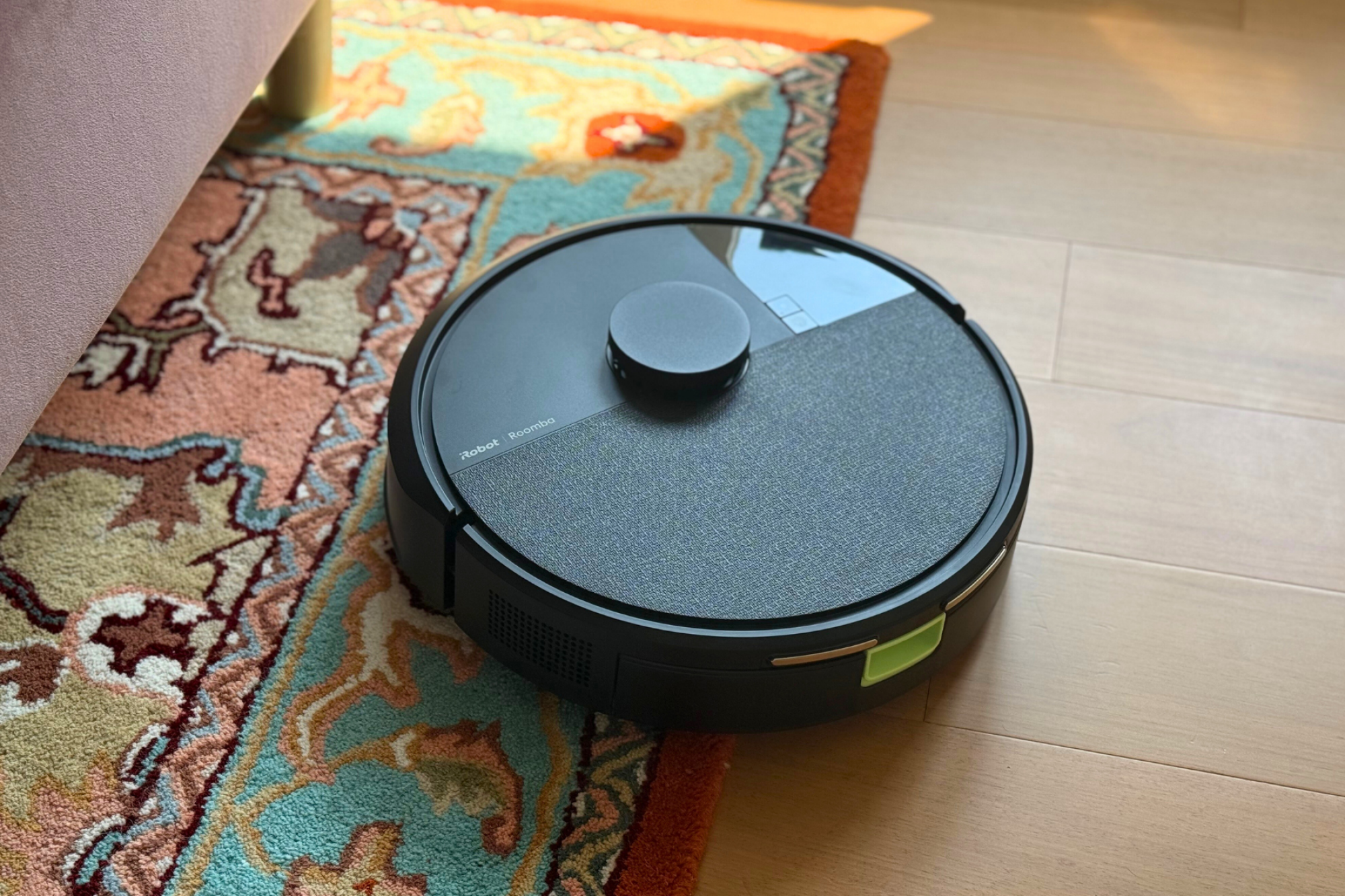 Roomba 105 robot vacuum cleaning rug and hardwood floor near bed frame