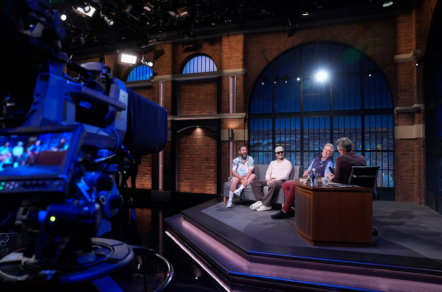 LATE NIGHT WITH SETH MEYERS -- Episode 1677 -- Pictured: (l-r) Comedian/actor Adam Sandler, rapper Bad Bunny, and actor Christopher McDonald during an interview with host Seth Meyers July 22, 2025 -- (Photo by: Lloyd Bishop/NBC)