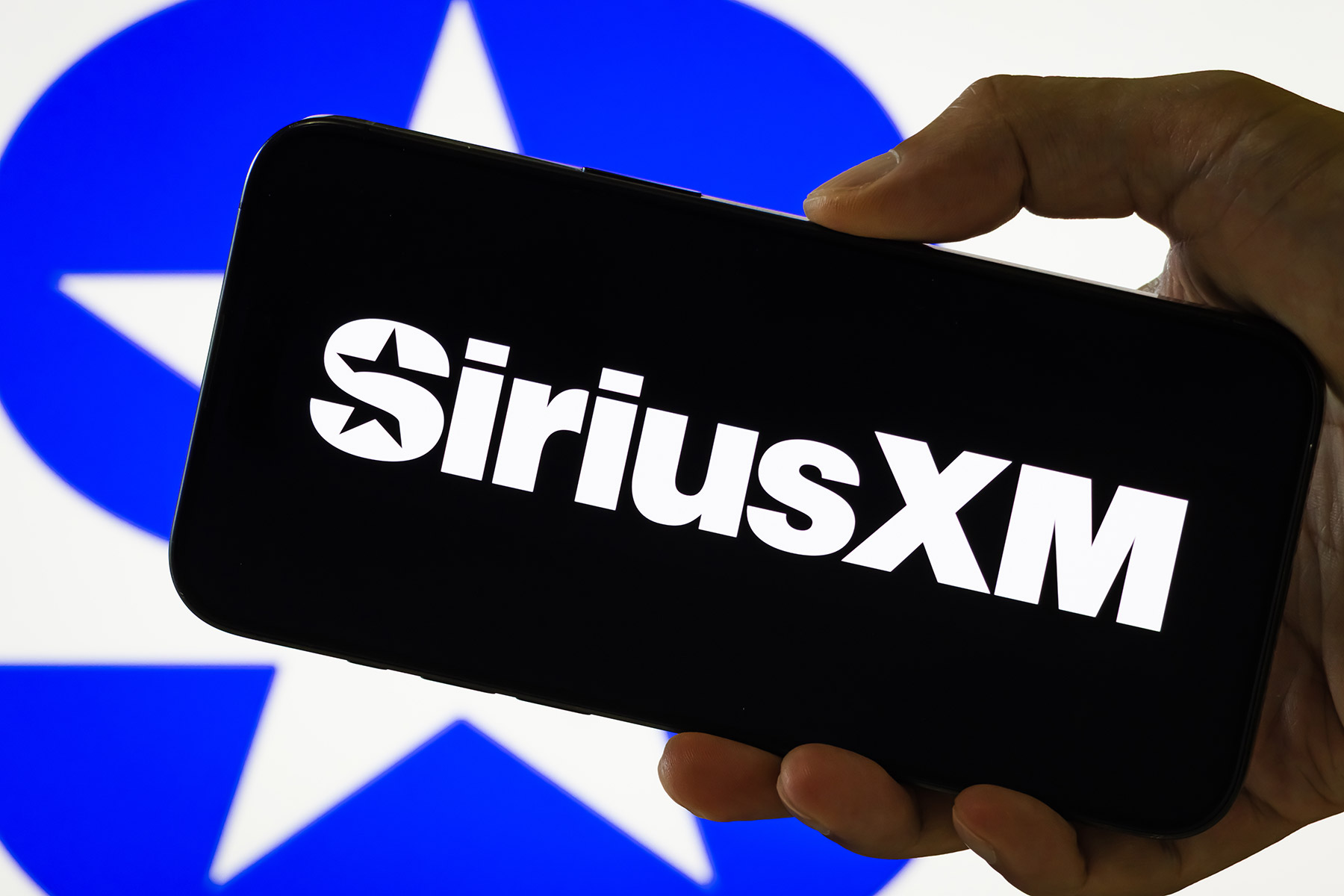 In this photo illustration, a person holds a smartphone displaying the logo of Sirius XM Holdings Inc.