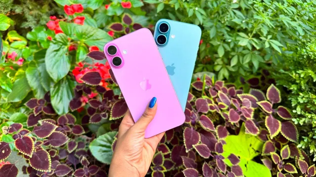 a woman holds the iphone 16 and 16 plus in front of a garden