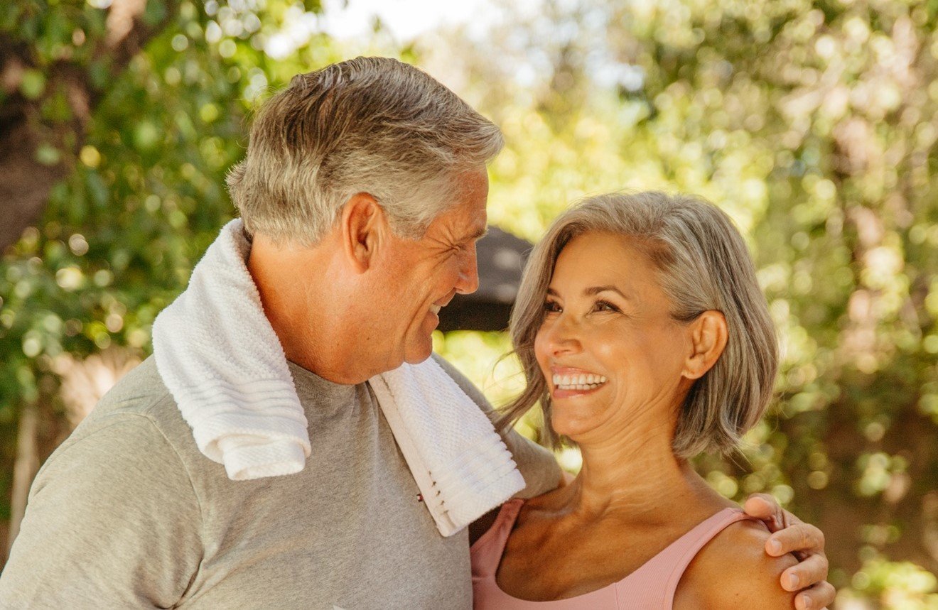 Happy couple enjoying a moment together outdoors, smiling and embracing, with greenery in the background.