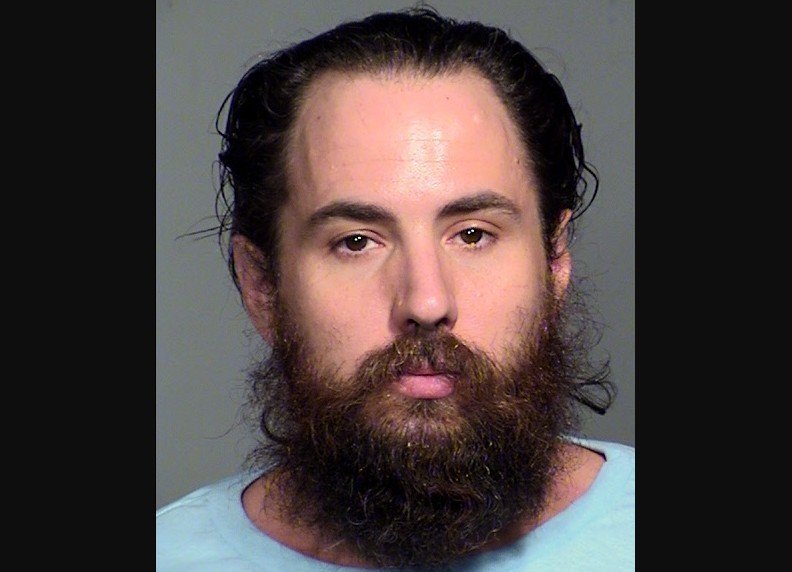 Mugshot of a man with long hair and a full beard, wearing a light blue shirt against a neutral background.
